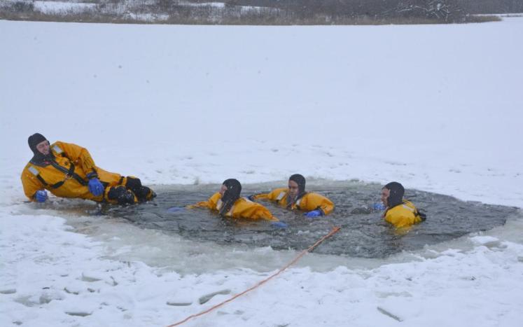four divers in yellow gear in open hole in ice on lake
