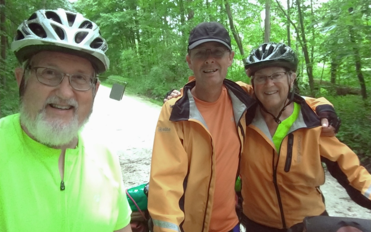 Three cyclists taking a selfie, Male on left with green shirt, Center Male with orange jacket and female with orange jacket