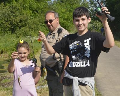 Boy and girl show up fish they caught with officer