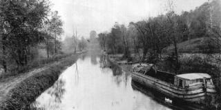 Historic black and white photo of the canal in Kent, including a canal boat along the right shoreline.