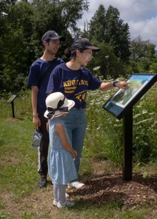 a family of three pauses to read a story trail sign