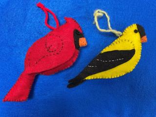 a red, felt cardinal and yellow and black felt goldfinch lay on a blue background 