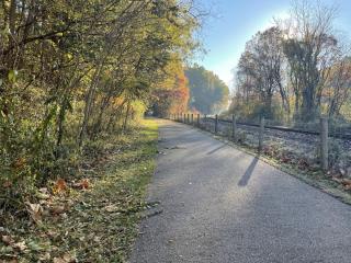 asphalt trail with trees on the left and fence next to railroad on the right