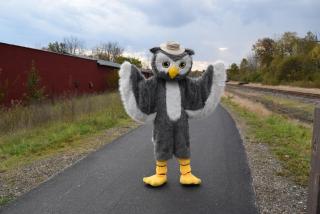 an owl mascot wears a tan park hat on a paved trail