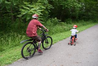 adult and child with bike helmets riding bikes on asphalt paved trail