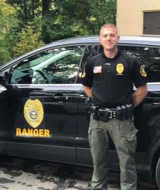 Chief Ranger Zach Steele stands in front of the black SUV with a park ranger badge decal.