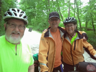 Three cyclists taking a selfie, Male on left with green shirt, Center Male with orange jacket and female with orange jacket