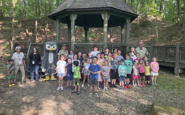 A group of kids poses with an owl mascot to receive their junior ranger badges.