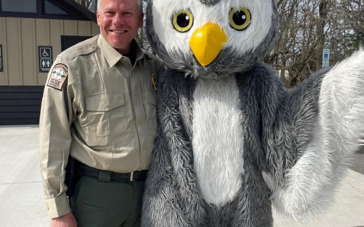 a park ranger poses with a fluffy owl mascot